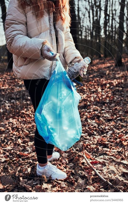 Young woman cleaning up a forest. Volunteer picking plastic waste to bags.  Concept of plastic pollution