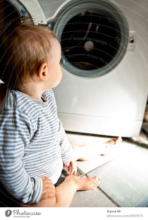 Baby toddler sits interested and curious in front of washing machine on the floor Toddler Washer Cute Child peril Observe inquisitorial Boy (child)