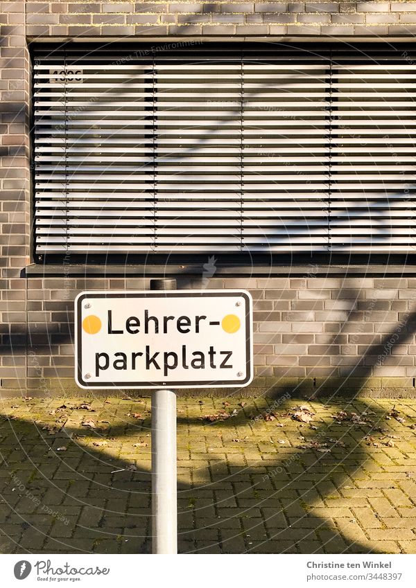 Empty parking lot. A sign 'Lehrerparkplatz' in front of a school building with closed shutters Signage Signs and labeling Characters Parking lot Reserved School