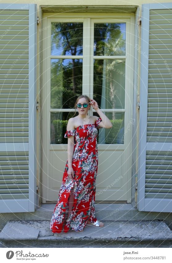 young woman in long summer dress and sunglasses standing in front of an old building door with open wooden shutters Young woman Summer Blonde Slim Feminine