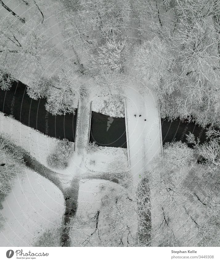 A snowy bridge with walking people high from above in a cold winter scenery. Snow vertical drone aerial tree river angle outdoors landscape park freedom run