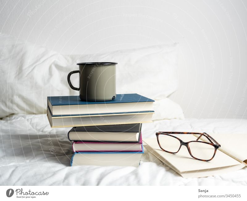 Bücherstapel mit einer Tasse Kaffee und einer Lesebrille auf einer weißen Bettdecke im Schlafzimmer bücherstapel kaffee getränk lesebrille bett bettdecke