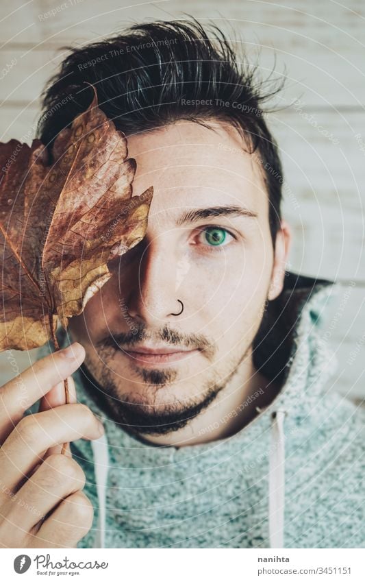 Young man covering his face with a dry leaf attractive cool male portrait autumn creative artistic beard piercing nose close handsome guy young youth lenses