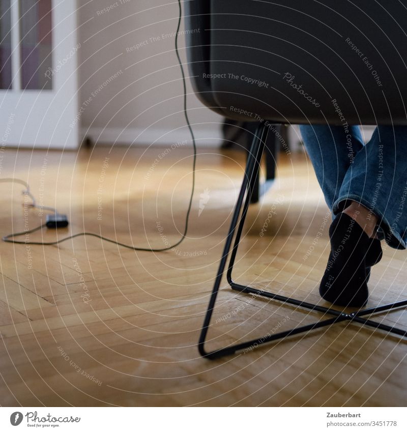 Legs of a woman sitting on a chair in her home office, with cable and power supply of her computer, on parquet floor Chair Sit feet socks Cable Power cord