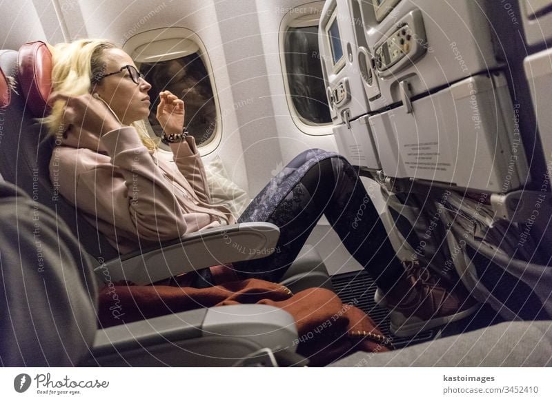 Sporty casual young blonde caucasian lady watching movie while traveling by airplane by the window. Commercial transportation by planes flight entertainment