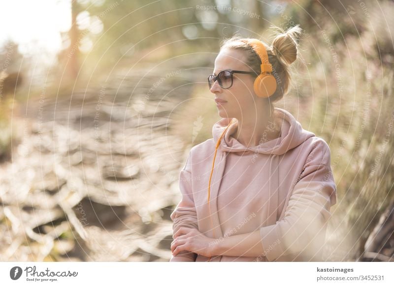 Portrait of beautiful sports woman wearing sunglasses, hoodie and headphones during outdoors training session girl portrait nature workout active runner