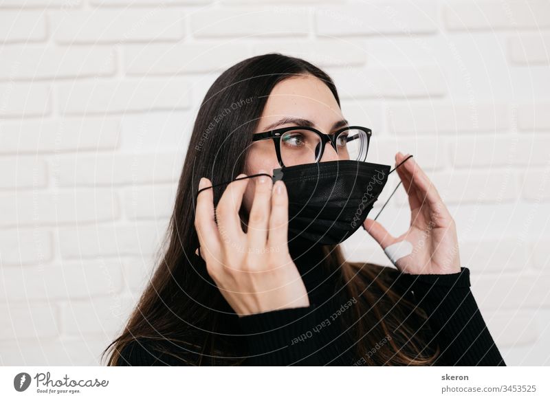 brunette girl in glasses for vision correction is protected from a viral infection: coronavirus. A woman in a black medical mask during the pandemic  2019-nCoV COVID. the patient in quarantine