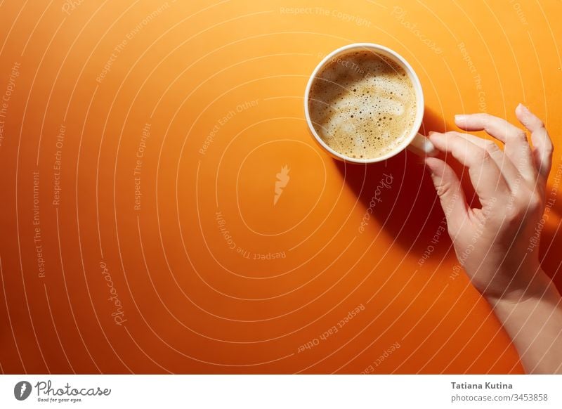 A cup of black coffee with a female hand on a bright orange background. Minimalism, top view. copyspace mug drink design cafe food hot breakfast paper white