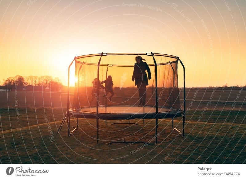 Trampoline on a lawn in the sunset with two kids recreation silhouettes dawn sunrays blond children balance action gymnastics sport garden positive girl