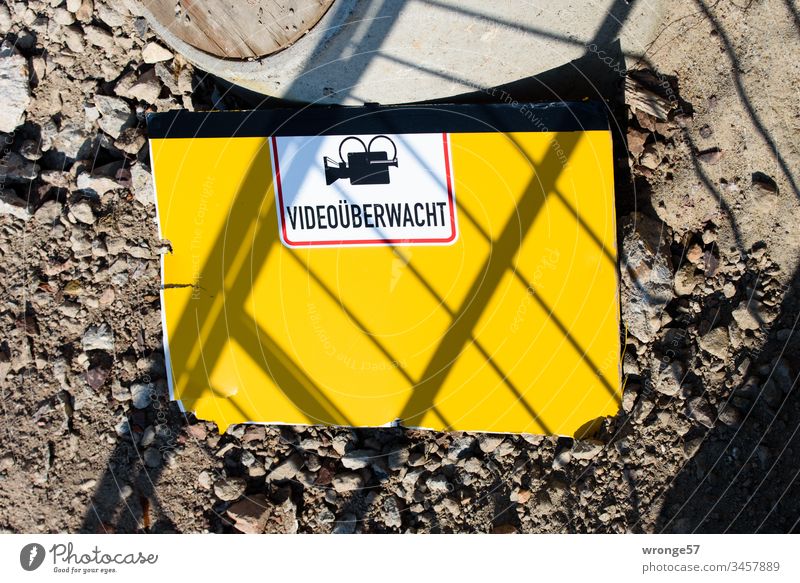 Yellow sign Video-monitored lies on the floor of a construction site Construction site Ground gravel Exterior shot Deserted Day Colour photo Work and employment