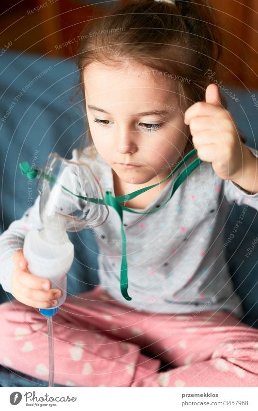 Sick little girl having medical inhalation treatment with nebuliser. Child holding breathing mask sitting in bed child virus infection doctor flu ill sick cold