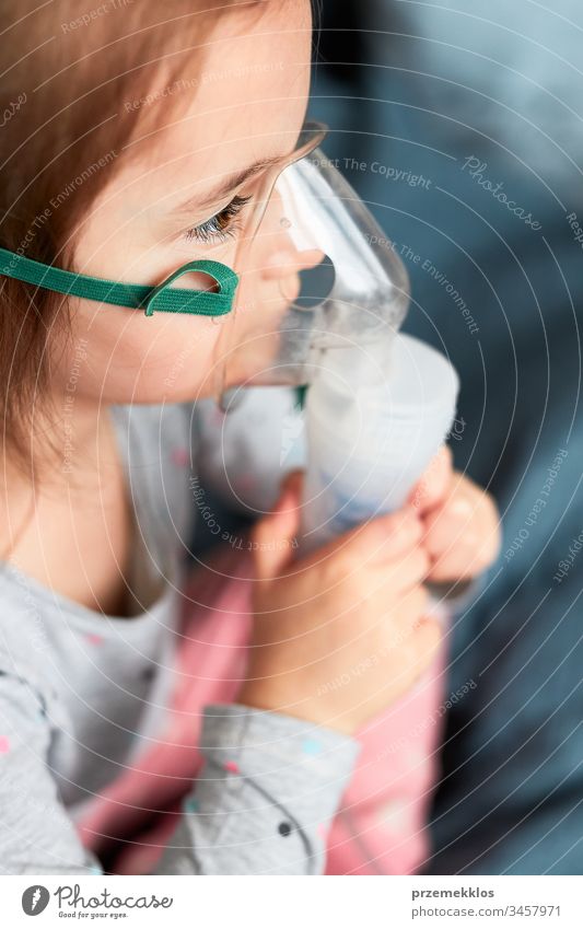 Sick little girl having medical inhalation treatment with nebuliser. Child with breathing mask on her face sitting in bed child virus infection doctor flu ill