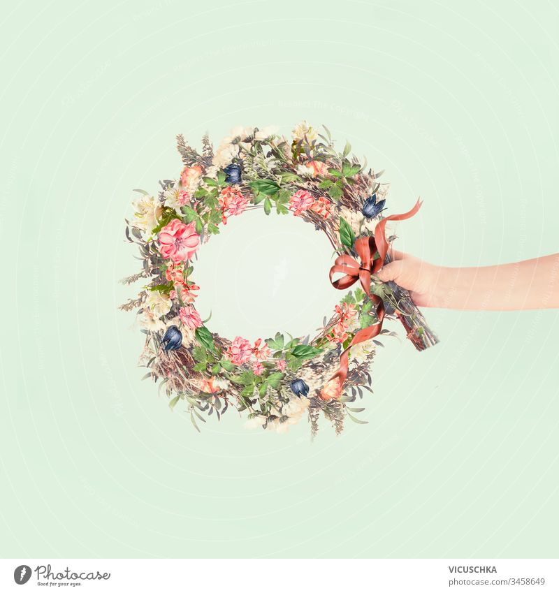 Female women hand holding summer flowers wreath with ribbon at light mint background. Creative flowers arrangement concept female creative anniversary art