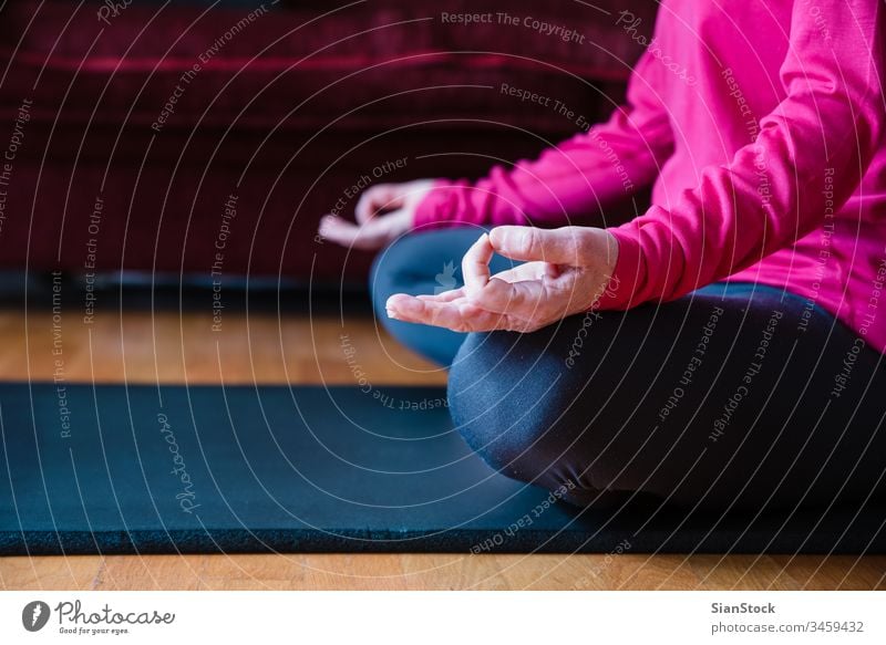 Hands close up of middle aged woman sitting in lotus position on yoga mat in her living room. bending beauty workout european exercising hands flexibility