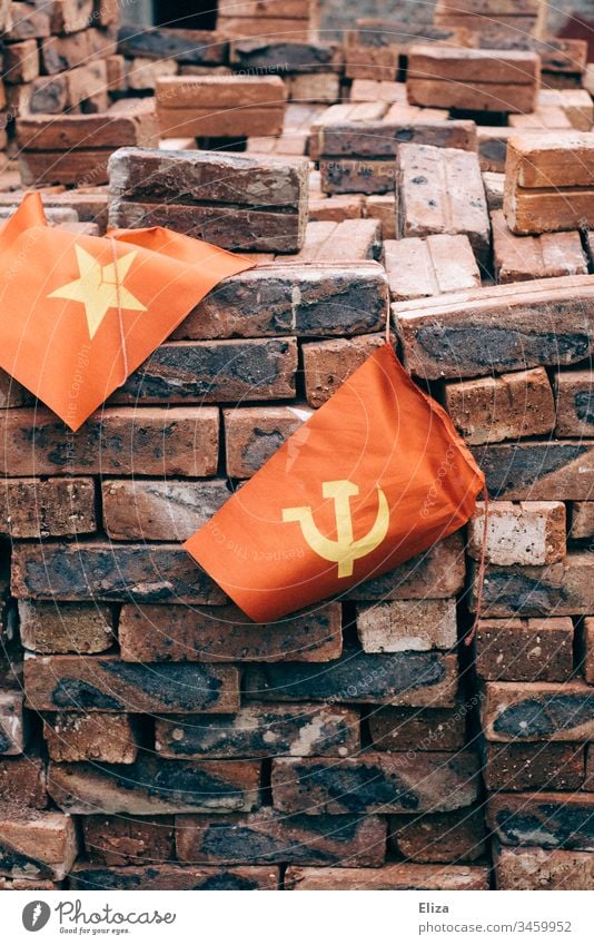 The Vietnamese flag next to a flag with hammer and sickle, symbolizing the communist state, in front of a pile of red bricks Communism Hammer Socialism Build