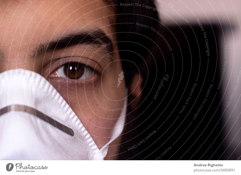 Half portrait of a young caucasian adult wearing a white mask. Copy space on the right. Man looking at the camera air boy care closeup coronavirus covid19