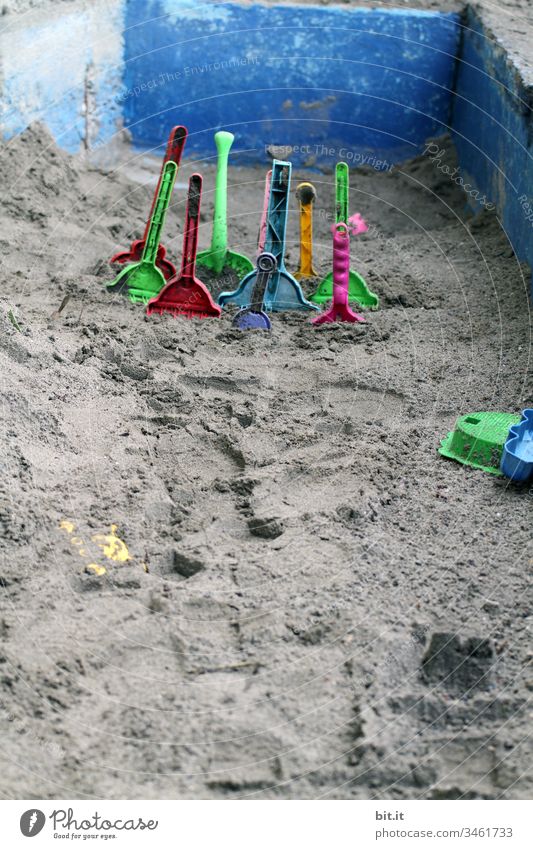 Many, colourful plastic sand shovels are stuck in the sand, in an empty sandbox of stone, on holiday. Sand Sandpit Sandal shovel Shovel Playing Toys Infancy