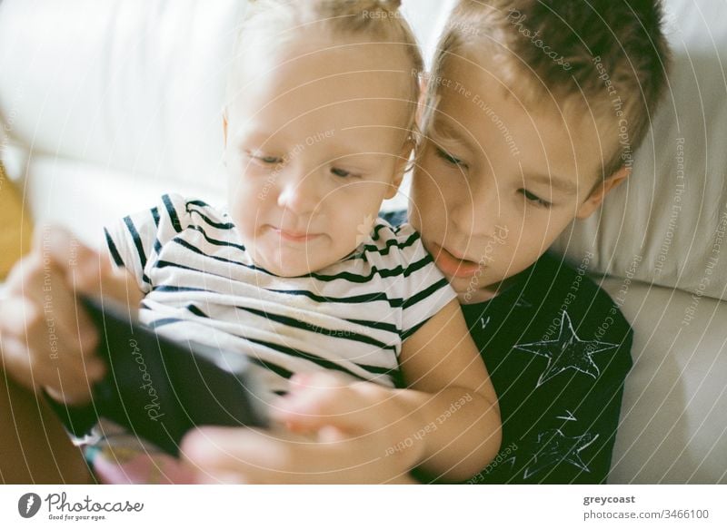 Kids spending home leisure with mobile games. Big brother looking after little sister and helping her play children fun siblings kid cellphone activity family