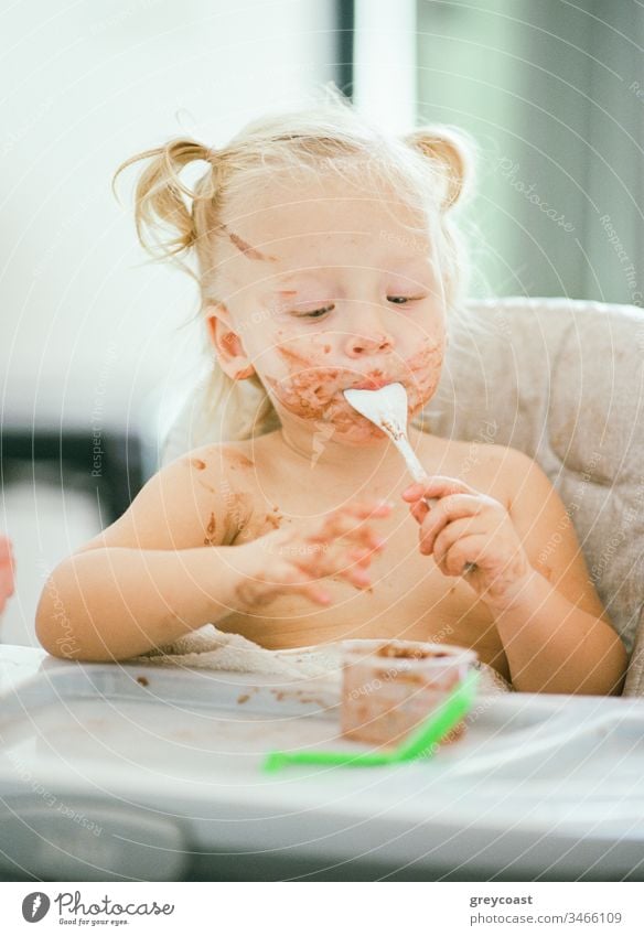 It does not matter how dirty your face is when it is so yummy. Little girl eating sitting in highchair kid messy eater breakfast child toddler portrait baby