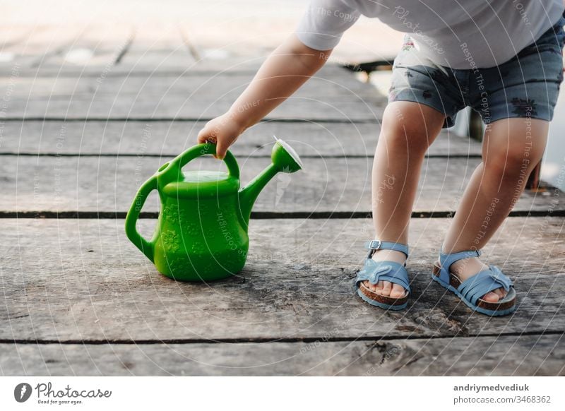 A small girl is playing with a watering can of a wooden bridge. Spring and summer. Gardening. green watering can baby little child cute garden background white