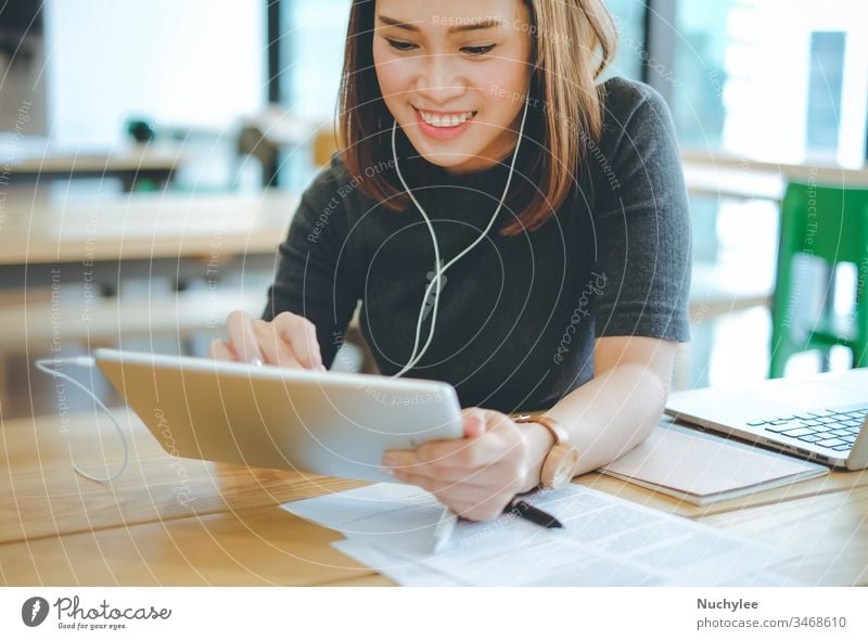 Young smiling asian businesswoman listening music and using tablet in office or cafe, lifestyle and business concept casual cheerful city communication computer