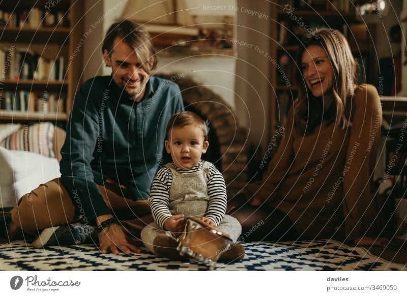 Young happy couple staying at home with their baby son sitting on the living room floor. lovely happiness man woman cheerful carpet smile growth caring boy