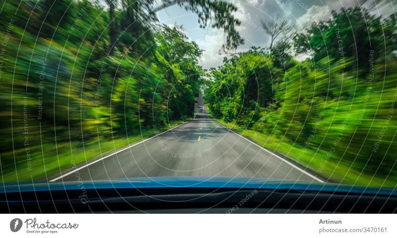 View from front of blue car on asphalt road and speed motion blur on highway in summer with green trees forest at countryside abstract art background blurred