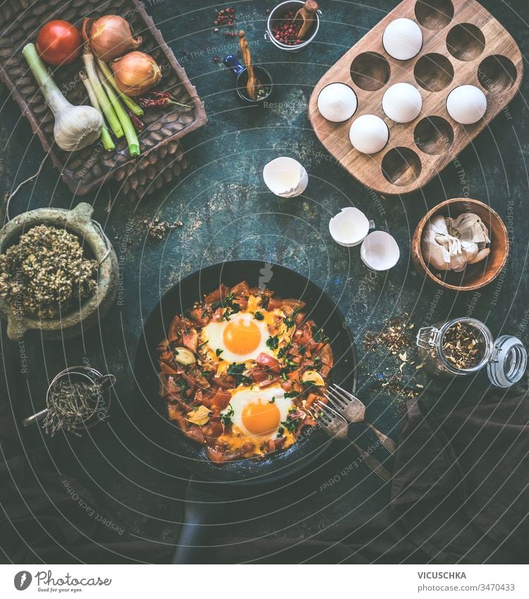 Tasty fried eggs in tomato sauce in black pan with fork on rustic background. Top view. Shakshuka breakfast. Ingredients. Cooking. Healthy food eating tasty