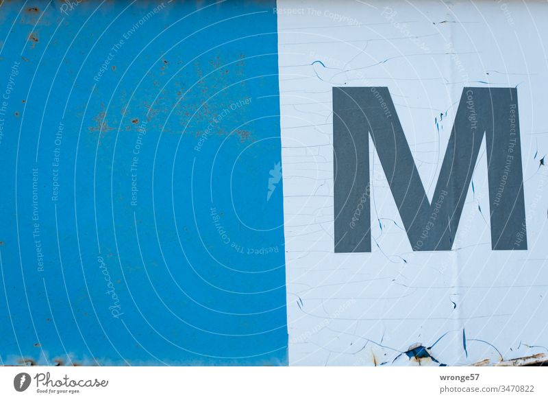 Capital letter M on white foil on a blue gate Letters (alphabet) Colour photo Day Characters Exterior shot Building Orientation Old weathered surface," blotchy