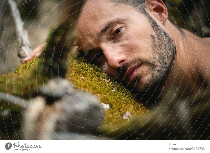 Portrait of a man lying on a tree trunk with moss in the forest and looking sad, melancholic, serious, vulnerable into the camera Man Tree Tree trunk Moss