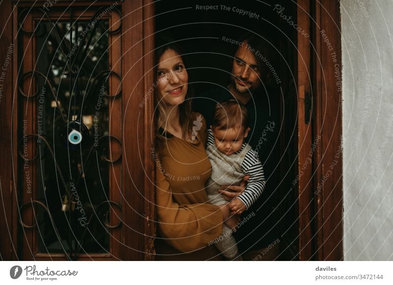 Family portrait of young man and woman holding their baby son at the entrance door of their home, with beautiful low light. 30s 30s couple estate father mother