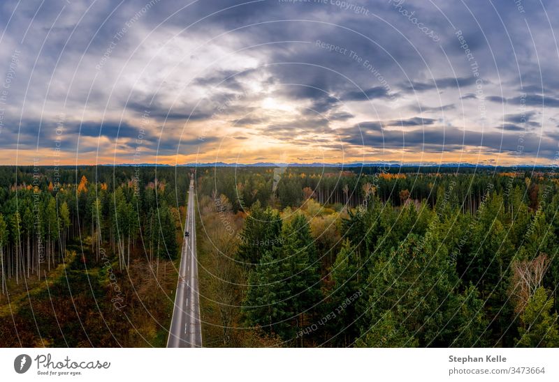 Aerial view of road among the forest and trees. Sunset field in southern germany near the alps. sunrise autumn aerial mountain fall drone above asphalt car