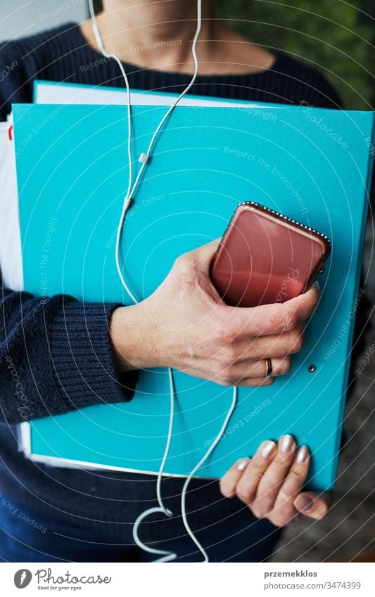 Woman working remotely doing job during call conversation on phone from home. Woman holding smartphone and documents in binder using headphones learning online