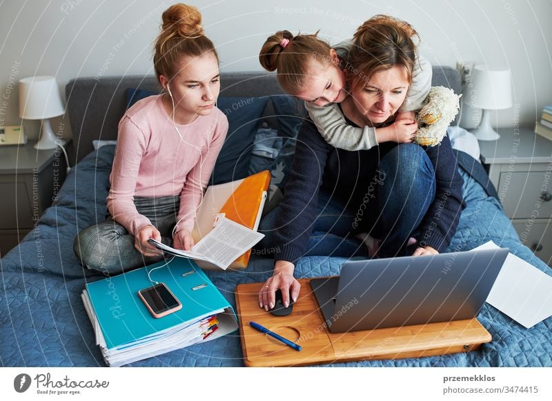 Women mother and daughter working learning remotely doing job homework during video chat call stream online course webinar lessons on laptop from home during COVID-19 quarantine. Women sitting on bed in front of computer looking at screen