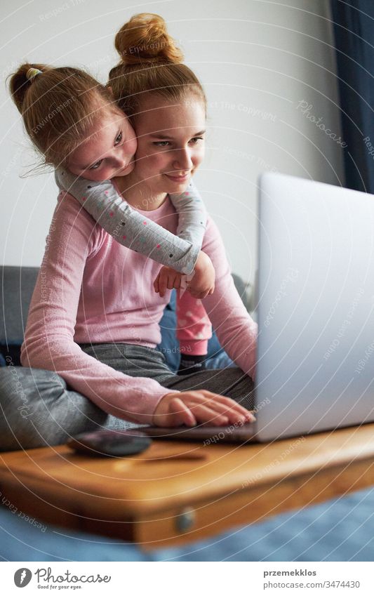 Grandchildren teenage girl and her younger sister talking on video call with granparents on laptop from home during COVID-19 quarantine. Girls sitting on bed in front of computer