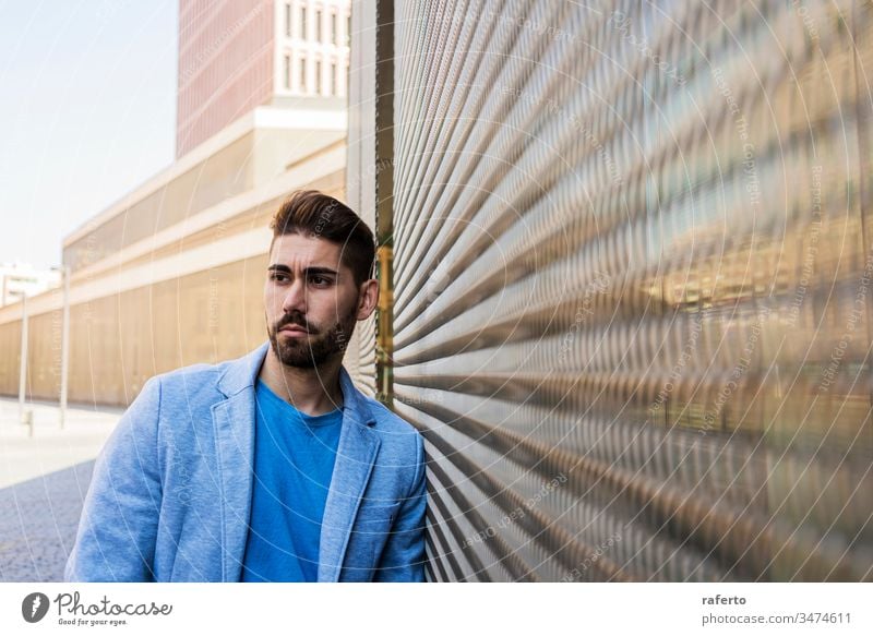Young bearded man, model of fashion, in urban background wearing casual clothes while leaning on a wall and looking aside cool style portrait guy 1 photogenic