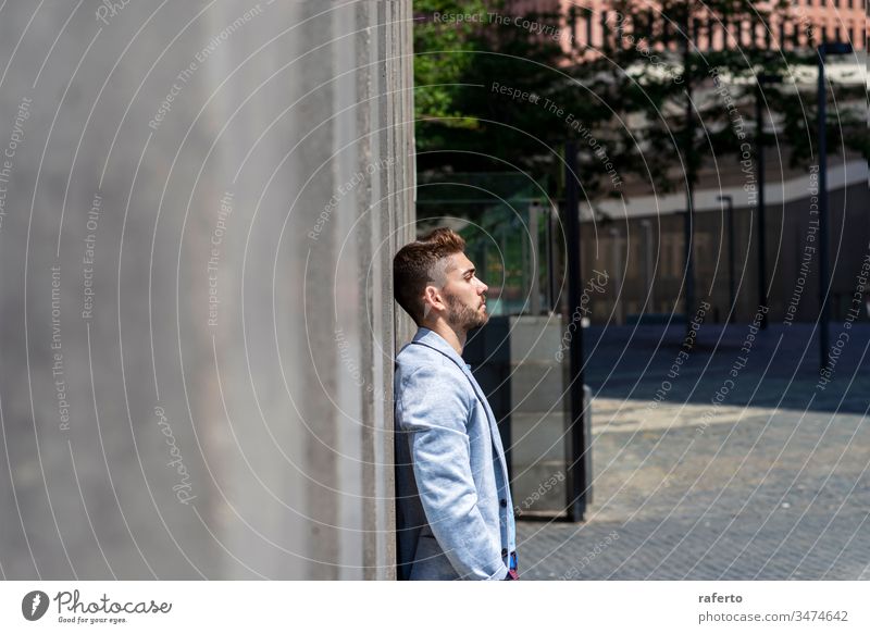 Pensive young bearded man looking away in the street while leaning on a wall outdoors uncertainty businessman thinking disappointment overworked professional