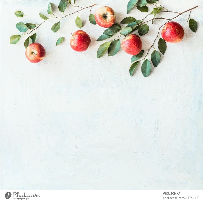 Tasty ripe red apples with branches and green leaves on rustic white background, top view. Border or frame with copy space for your design tasty border