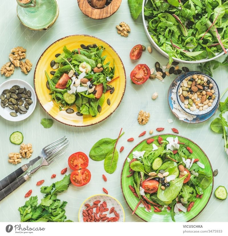 Plates with green salad on kitchen table background with forks and ingredients: nuts, seeds, young leaves, olives oils dressing. Top view. Dieting. Summer cuisine. Healthy home food