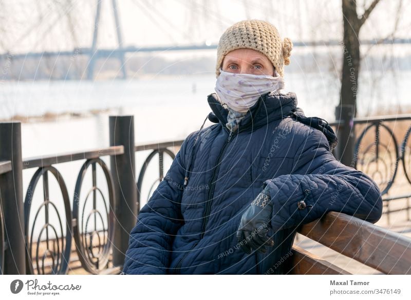 A poor elderly woman wears a homemade mask to protect herself from viruses adult bench breathing coat contagion contagious corona coronavirus cough country