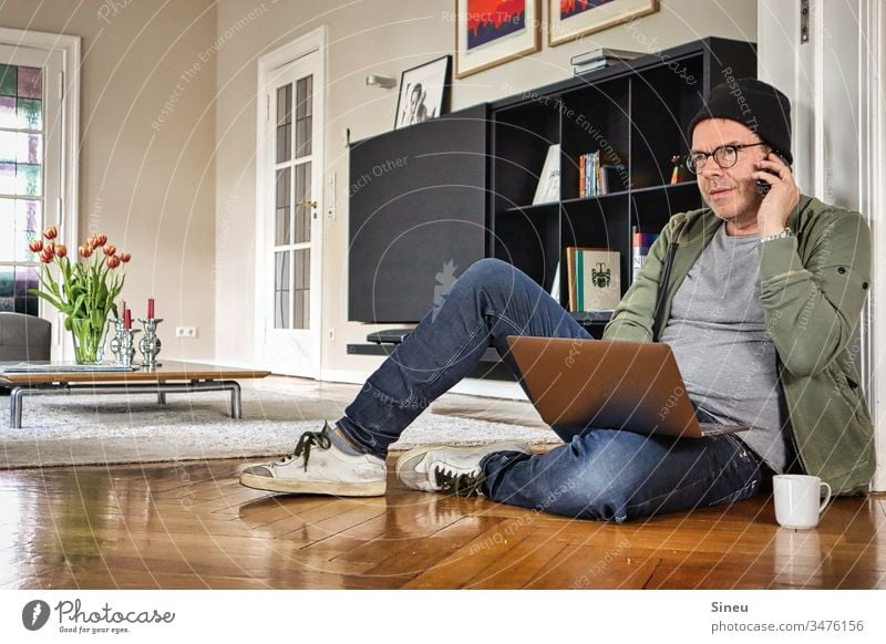 HomeOffice: the relaxed man is sitting on the floor in front of his notebook again and is looking forward to his office Living room work from home Home office