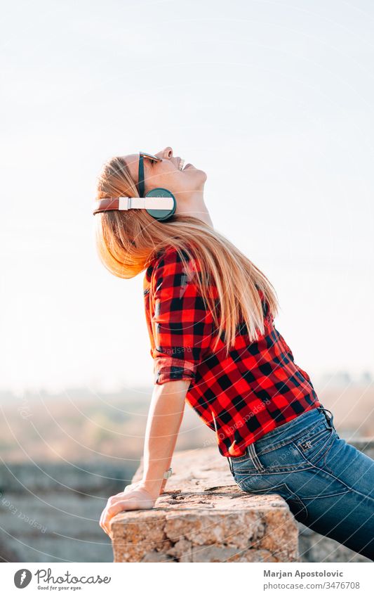 Young woman listening to the music with headphones outdoors in sunset young outside enjoying joyful wireless technology casual lifestyle cool mobile adult