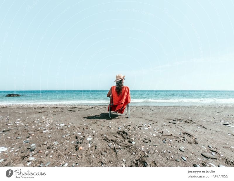 Girl in hat sitting on a lounger with orange towel on the shore of the beach background beautiful blue calm chair coast environment female freedom girl holiday