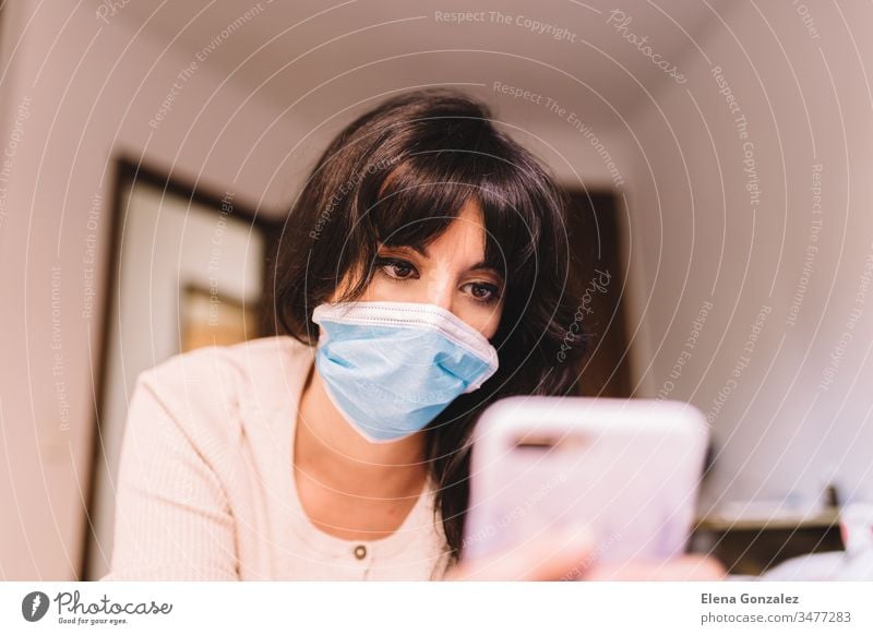 Female at home in breathing medical respiratory mask on her face using mobile phone. Chinese pandemic coronavirus, virus covid-19. Quarantine, prevent infection concept. Focus on her face.