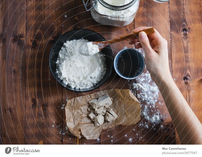 A woman's hand adding flour to make sourdough. Bakery concept. Sourdough Dough knead spoon yeast processing glass jar homemade wooden bottom dark background
