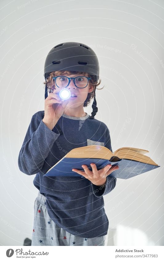 blond kid in pajamas with a helmet a flashlight and a book playing research children game protect happiness enjoyment room indoor party comfort emotional