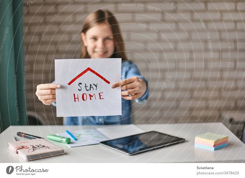 A beautiful teenage girl holds a sign saying stay at home. The girl recommends staying at home during the quarantine. Self-isolation, social distance childhood