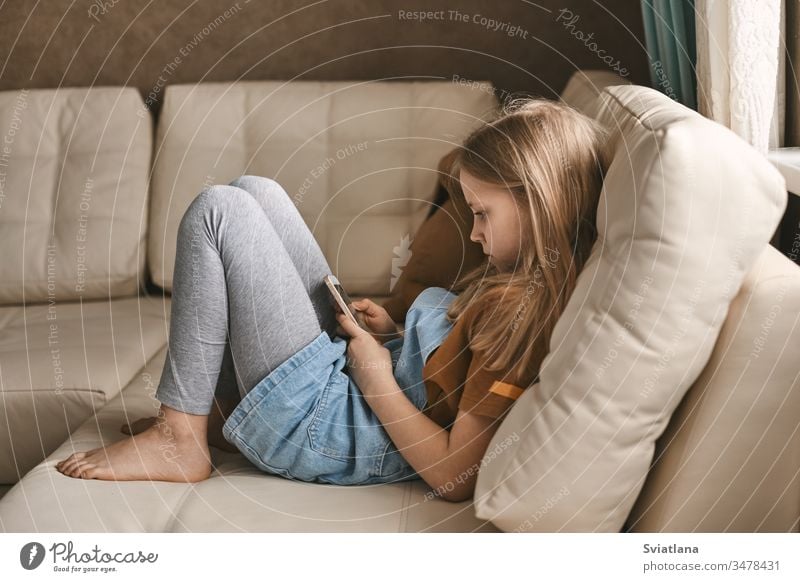 A pretty girl communicates with her friends via messenger during the quarantine. Self-isolation, communication, social distance during quarantine sofa