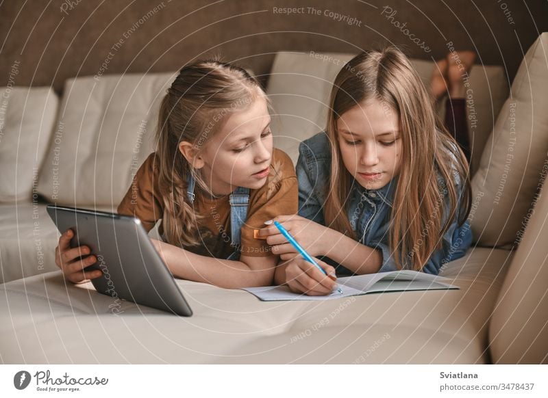 Two beautiful sisters do their homework during quarantine. Children use gadgets for learning. Education, distance learning, home schooling during quarantine