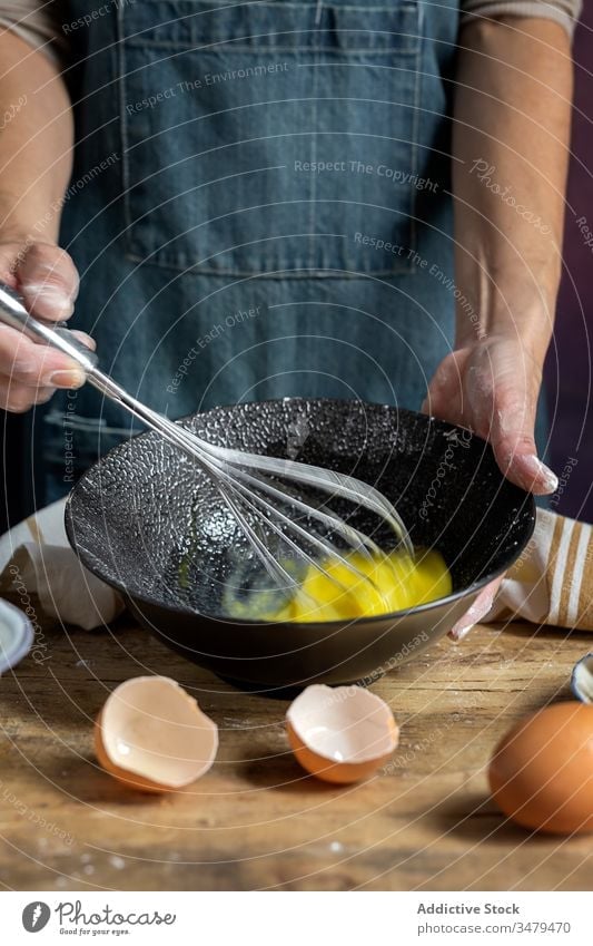 Faceless woman preparing eggs with whisk in kitchen cook ingredient bowl wooden table process food prepare cuisine fresh recipe delicious nutrition culinary